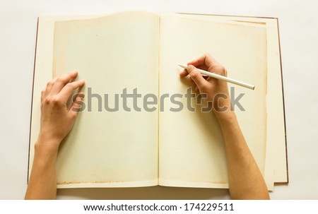 Human hands writing on blank pages of opened vintage book made of parchment