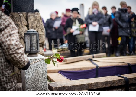 Group of mourners staying by the opened grave at a cemetery during a funeral ceremony