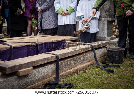 Mourners staying by the opened grave, burying a coffin at a cemetery during a funeral ceremony