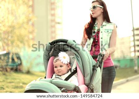 Modern mother with her baby walking down the street. Special warm color tuning.