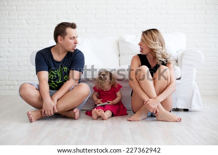 Mother and father showing a tongue while their daughter playing with phone