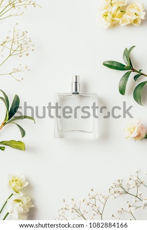 top view of bottle of perfume surrounded with flowers and green branches on white