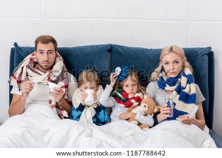 sick young family sitting in bed together and looking at camera