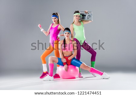 happy sporty girls with sports equipment and tape recorder on grey