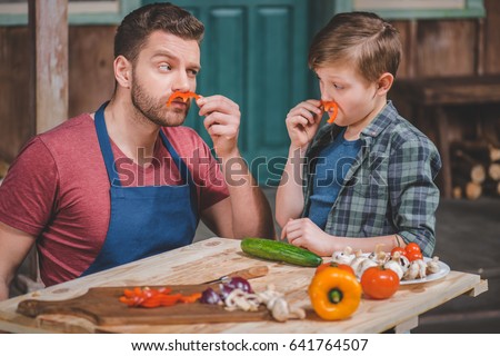 Father in apron and cute little son having fun with pepper moustaches, dad and son cooking concept