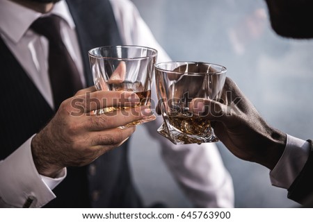 Close-up partial view of two men in formal wear clinking whiskey glasses