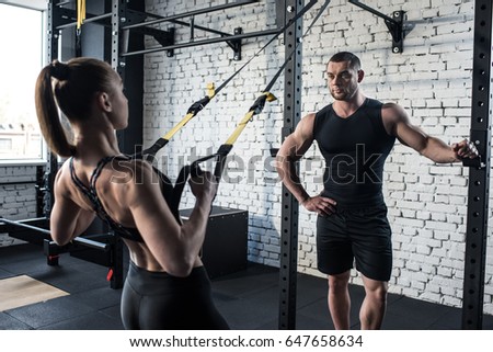 sportswoman training with trx resistance band with serious trainer in sports center