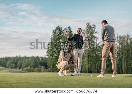 stylish multicultural friends spending time together while playing golf on golf course