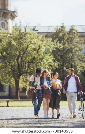 group of smiling multicultural students walking in park together