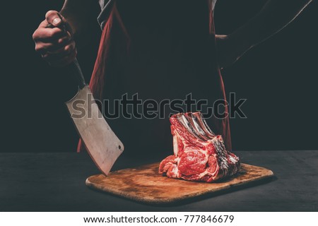 butcher with cleaver and raw meat on wooden cutting board