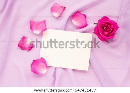 Pink rose, rose petals and empty paper on lilac background. Valentine\'s Day. Flat lay, top view.