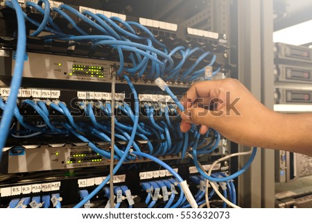 A man holds server cable in Server rack with blue internet patch cord cables connected to black patch panel in server room