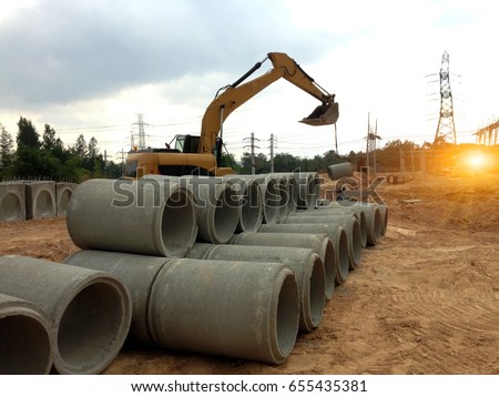 Focus on concrete pipes and backhoe to construct drainage systems on large power plant projects.Cement drainage pipes for industrial building construction,selective focus.