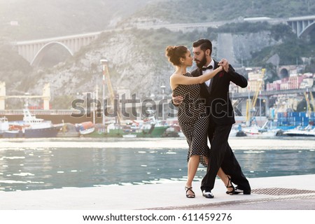 Young couple of sexy beautiful dancers, performing argentine tango dance steps on the dock in the port of Salerno, Italy. Sunset light, vintage retro look.