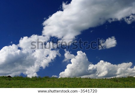 Beautiful green meadow under vivid blue sky dotted with fluffy white clouds.