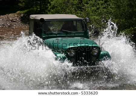 Popular four-wheel-drive vehicle plows through mountain stream creating large spray of water