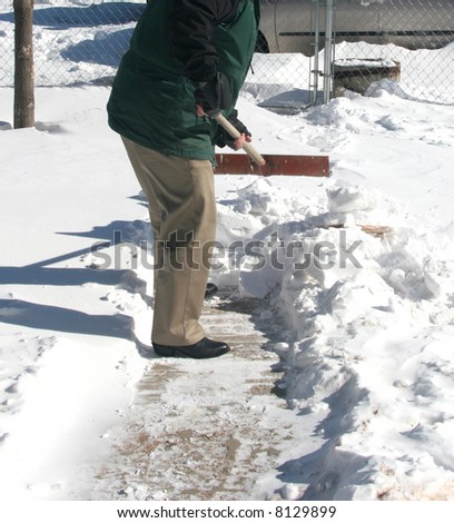 Homeowner shoveling snow on front walkway after winter storm to get to snow-covered driveway.