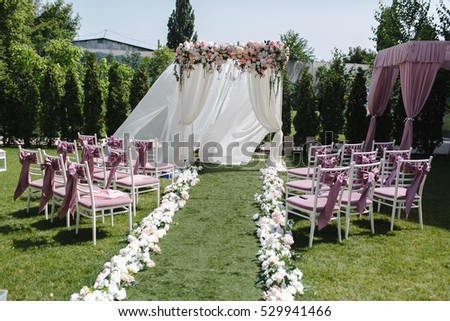 Simple decor for the wedding. Many pink and white chairs arranged on the lawn green. Ark adorned with flowers. A summer day.