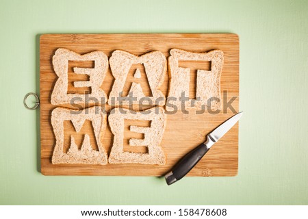 Eat me text carved out of brown bread slices on wooden chopping board with chef\'s kitchen knife, hunger, hungry