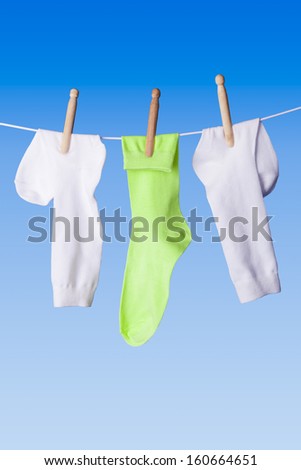 White and green socks with wooden clothes pins dolly pegs hanging out on washing line against blue background