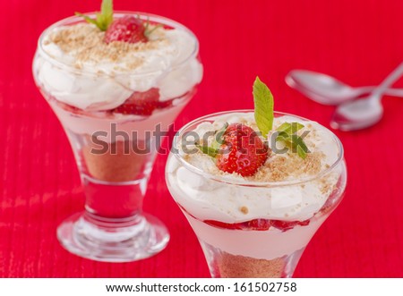 Two strawberry and cream desserts on red background with spoons for concept of love and romantic sharing