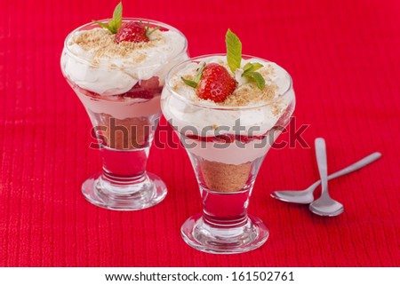 Two strawberry and cream desserts on red background with spoons for concept of love and romantic sharing