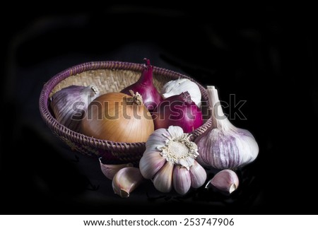 garlic, spring onion and brown onion in basket on black background