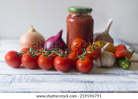 Fresh homemade tomato pasta sauce in jar with all ingredients of garlic,brown and red onion, colorful mini bell peppers with shallow depth of field
