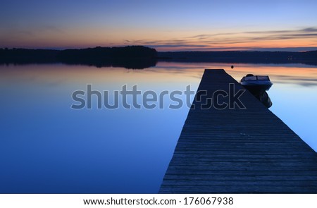 Wooden Dock with Small Boat on Calm Lake at Sunset