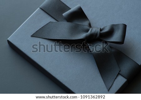 Black gift box on a dark contrasted background, decorated with a textured bow and feathers, creating a romantic atmosphere. Typically used for birthday, anniversary presents, gift cards, post cards.