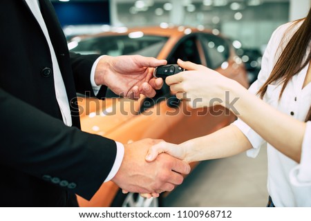 The visit to the dealership ended with the purchase of a car. The seller hands over the keys to the buyer on the back of a car dealership