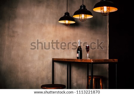 Interior design of restaurant or cafe. Side Photo of wooden table with bottle champagne or wine and glass with drink on it, three modern lamps above table