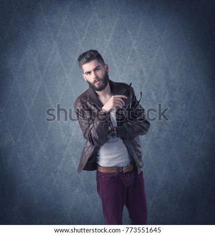 A handsome fashion model with beard standing in front of fancy background and making funny faces while using a vintage camera concept