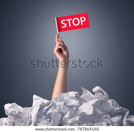Female hand emerging from crumpled paper pile holding a red flag with stop written on it