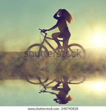 Girl on a bicycle in the sunset reflected on the water surface.