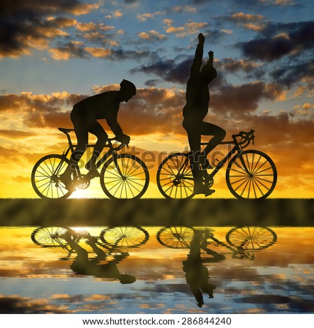 Silhouette of two cyclists riding a road bike at sunset