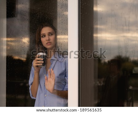 beautiful young woman with coffee cup looking through the window