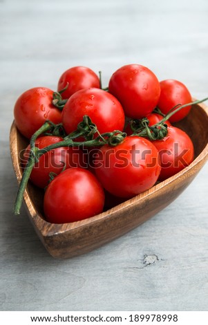 fresh red delicious tomatoes  in the heart shape wooden plate on an wooden tabletop, selective focus