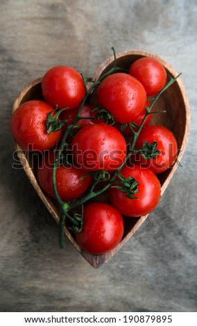 fresh red delicious tomatoes    in heart-shape plate on an  old wooden tabletop, selective focus