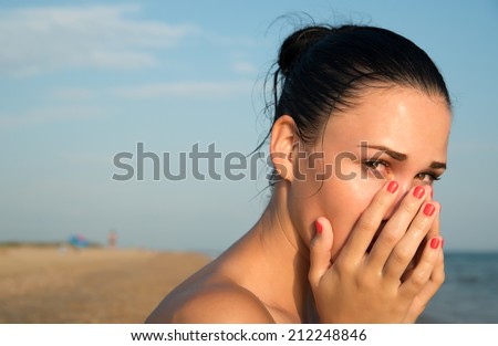 Close-up of a young woman with red eye  rubbing  irritated sensitive eyes or nose on the beach, allergy reaction
