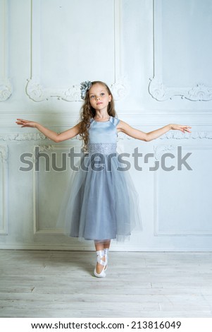 A little adorable young ballerina in beautiful dress and ballet shoes  dancing on her toes in the interior studio. Little Princess.