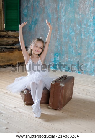 Little adorable ballerina in white tutu with old vintage suitcase in a beautiful studio. Travel and voyage. Concept of growing up, age, young and old.