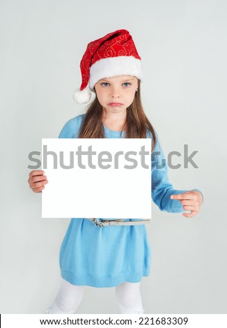 Cute girl in Santa Claus hat with a white blank paper sheet. surprised, puzzled, frustrated, sad facial expression. Christmas, x-mas, New Year, Winter, people, advertisement, sale concept.