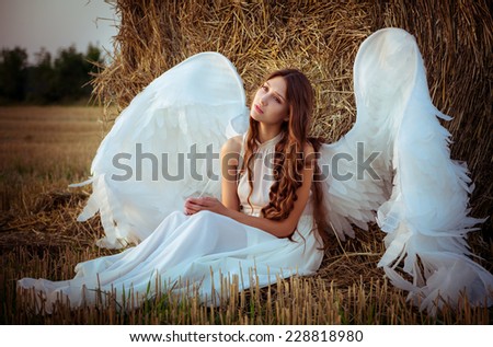 beautiful girl with angel wings is sitting front of the hay on the field in the morning.