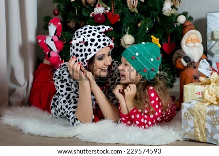 Mother and daughter in festive home clothes under the Christmas tree smiling and talking