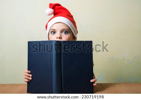 Cute girl in Santa Claus hat with big blue book.  Christmas, x-mas, New Year, Winter, people, advertisement, sale concept. Education concept.
