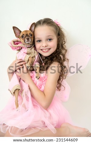 blond little girl in pink fairy costume holds small pet dog.