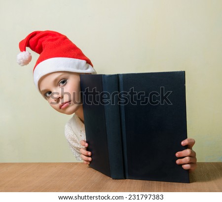 Cute girl in Santa Claus hat with big blue book.  Christmas, x-mas, New Year, Winter, people, advertisement, sale concept. Education concept.