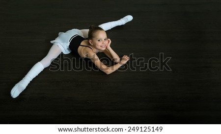 A little adorable young ballerina doing stretching exercises on the floor. Ballet,  gymnastics, free callisthenics.