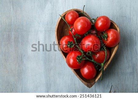fresh red delicious tomatoes  in the heart shape wooden plate on an wooden tabletop with place for text. Selective focus, close up.